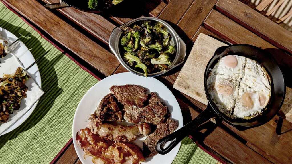 plate of steak, bowl of grilled broccoli, and pan of fried eggs