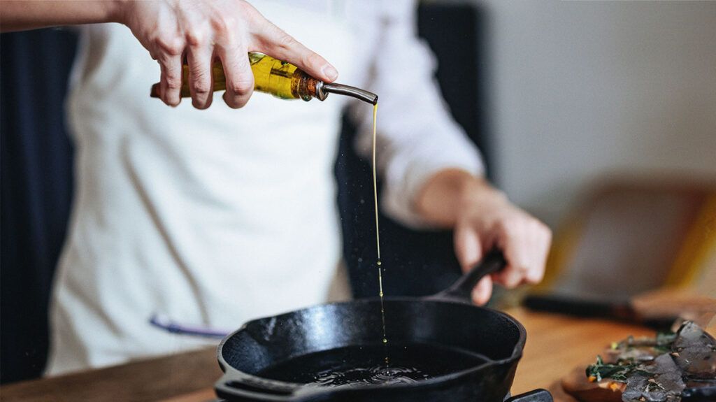 A close-up photo of a person pouring olive oil in a frying pan